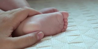妈妈手里抱着宝宝的脚。新生儿在女性父母手中。小孩子的脚在妈妈的手掌里。特写镜头。孩子的小脚趾和快乐父母的女人的手。母亲节的节日。