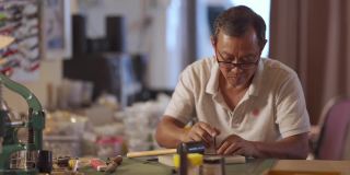 一位亚洲华人老人在他的工作室里制作手工皮革表带