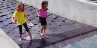 两个女孩在瀑布般的城市喷泉上戏水
