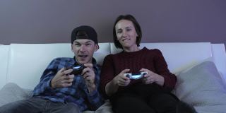 微笑快乐的朋友拿着游戏手柄在家里玩电子游戏。快乐的情侣在客厅的沙发上玩游戏，用无线控制器放松