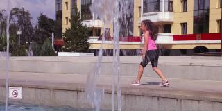 一个女孩走在城市喷泉的水柱后面