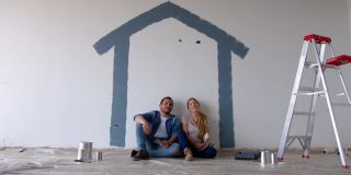 幸福的夫妇在画完画后休息一下，坐在地板上指指点点，看着他们装修的房子，男人拥抱着女人