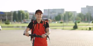 微笑的亚洲男人带着红色热背包送餐，骑着电动车走在街上。积极送货员工人员工送货在线订单客户客户