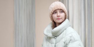 忧郁少女的肖像在城市侧视。可爱体贴的十几岁女孩，穿着暖和的夹克，戴着针织帽子，看着外面