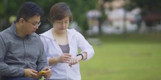 亚洲华人中成年夫妇在公园长凳上锻炼后，使用健身追踪器移动应用连接到健身追踪器