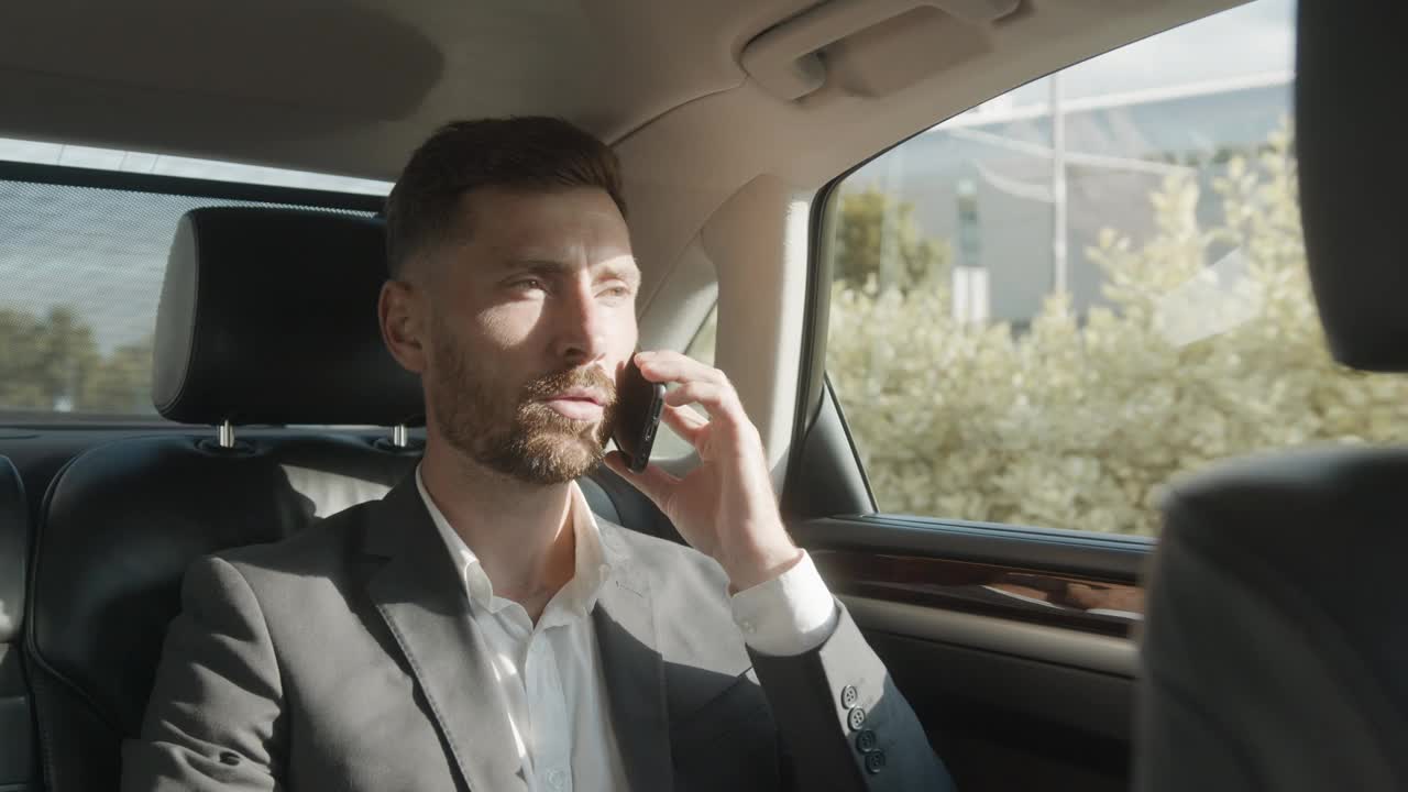 一位自信的商人在商务舱旅行时正在打电话。一个英俊的白人男性坐在他的豪华轿车里，和他自己的司机一起。成功的生活方式