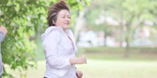 慢动作侧视亚洲华人中成年夫妇穿着运动服奔跑微笑着看向公园