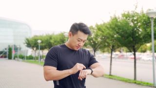 运动亚洲人看智能手表在现代轨道。男子跑步使用智能手表手链。视频素材模板下载