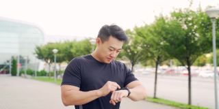 运动亚洲人看智能手表在现代轨道。男子跑步使用智能手表手链。