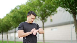 运动亚洲人看智能手表在现代轨道。男子跑步使用智能手表手链。视频素材模板下载