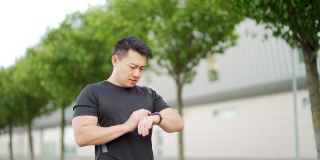 运动亚洲人看智能手表在现代轨道。男子跑步使用智能手表手链。