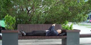 亚洲商人办公室职员放松地躺在长椅上，手里拿着手机