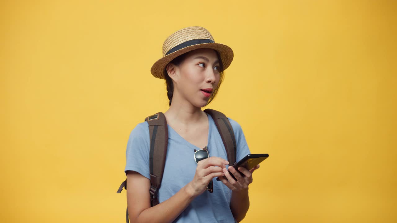 快乐青春美丽亚洲女人戴着帽子和背包持有智能手机享受预订旅行旅行酒店和机票书。