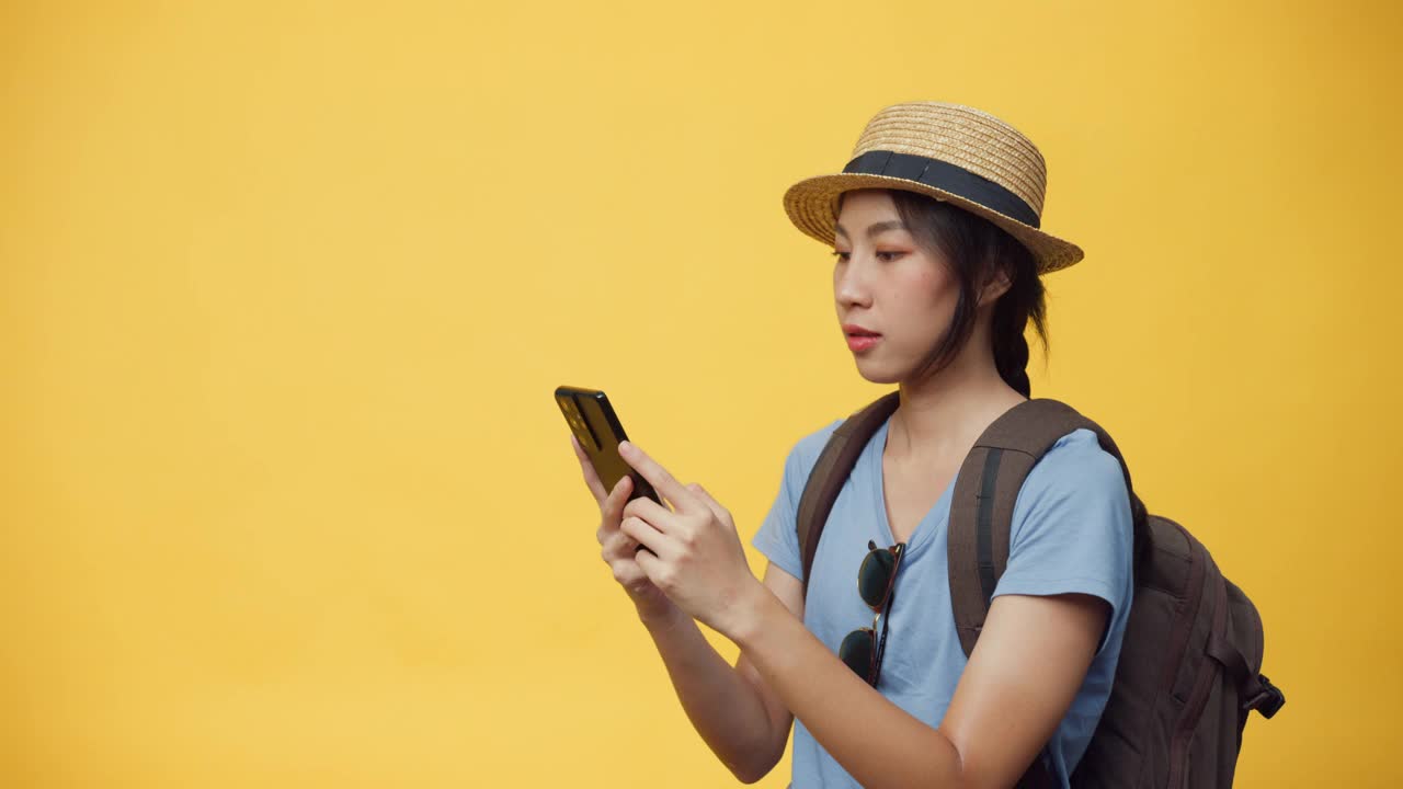 快乐青春美丽亚洲女人戴着帽子和背包持有智能手机享受预订旅行旅行酒店和机票书。