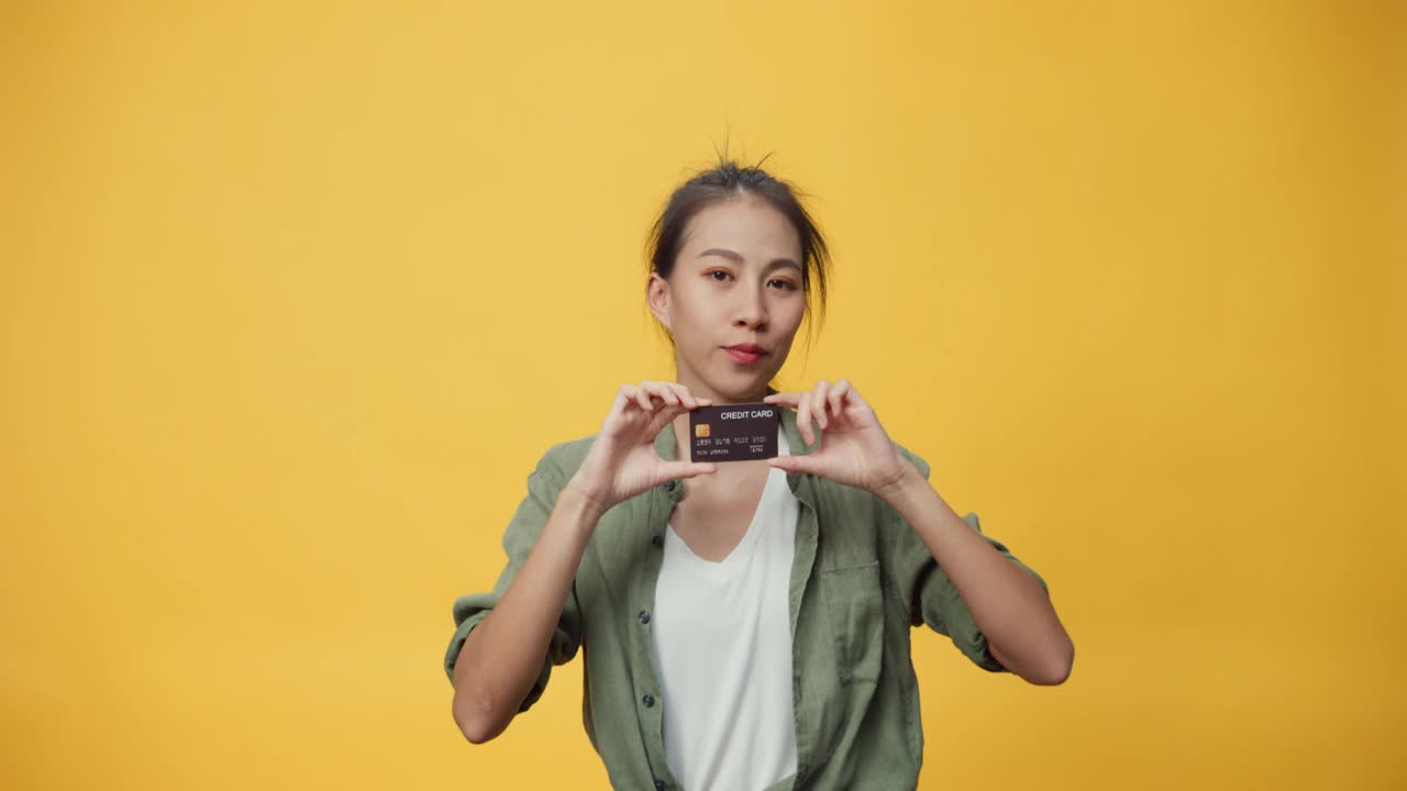 美丽迷人的亚洲青年孤立的女士手握信用卡惊奇的礼物购买网上电子购物与成功支付在黄色背景。