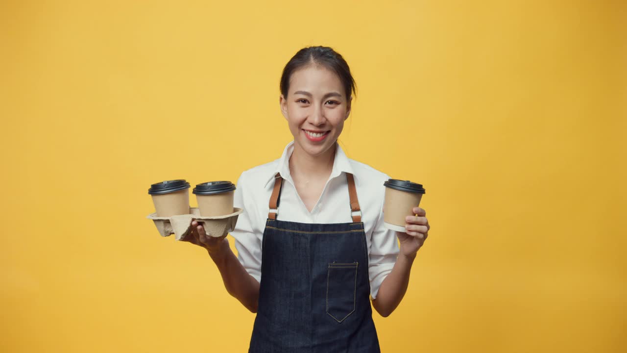 快乐微笑的亚洲女服务员正准备为顾客点菜，同时看着隔离在黄色背景上的相机。