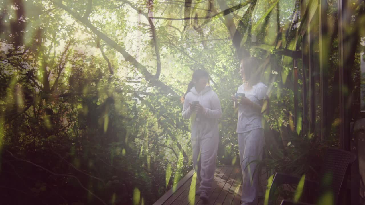 两个快乐的亚洲女人，捧着茶，漫步森林，动着草，徜徉大自然