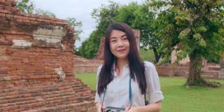 开朗美丽的年轻亚洲背包客博主女人随意带着相机微笑着在古城宝塔周围旅行。