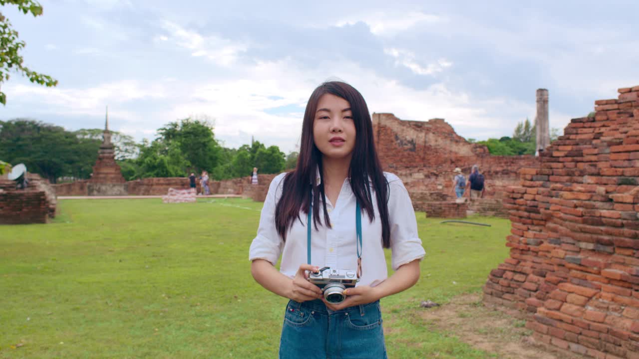 开朗美丽的年轻亚洲背包客博主女人随意带着相机微笑着在古城宝塔周围旅行。