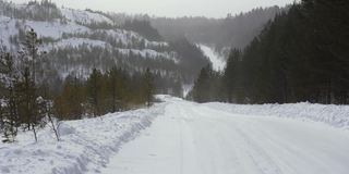 在多云的冬日，山坡上冬季道路的景象。镜头。一场暴风雪在一个冬天的老采石场的小路上的第一人称视角