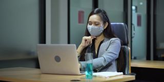 亚洲女雇员戴着口罩使用笔记本电脑在商业办公室工作与同事保持社交距离保护冠状病毒或covid-19爆发大流行。职场新常态政策