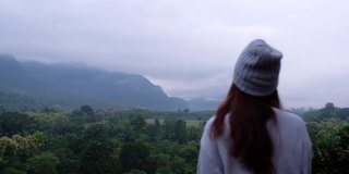 模糊的慢镜头，一个女旅行者在雾天看美丽的山景时挥手
