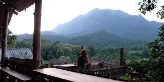 一位女游客坐在木制阳台上，看着美丽的山景