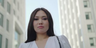 自信的年轻亚洲多种族女性看着相机站在商业区。严肃的千禧休闲职业女性戴上眼镜，离开。