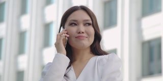 微笑的亚洲女人穿着正式的西装使用手机打电话外商业手机城市智能手机。
