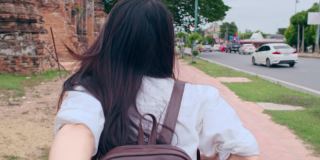 年轻的亚洲背包客女博主拿着相机，牵着男友的手，带着幸福的微笑，兴奋地在旧城街道一起旅行。