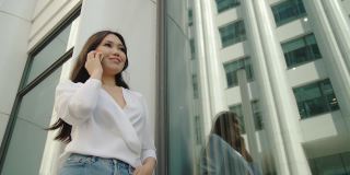 亚洲女商人在电话交谈愉快的实习生电话在商业区。微笑的独立女性享受成功的事业。风移动头发。