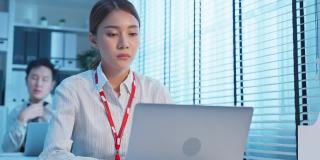精疲力竭的亚洲生病的企业女工在办公室的桌子上工作。员工在工作到很晚，在工作场所的电脑桌上过度工作，会感到疲惫和头痛。