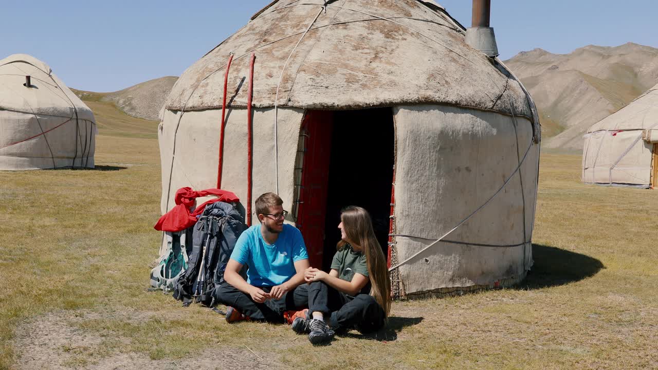 年轻的男女背包客早上在吉尔吉斯斯坦的蒙古包营地相遇