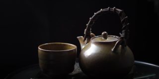 将热茶倒入玻璃茶壶和杯子中，木制背景上有蒸汽。健康热茶概念