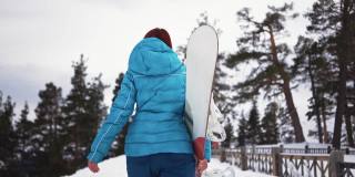 女孩在雪地里手拿滑雪板走路。冬季户外活动