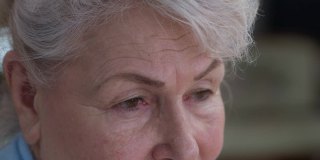 闭上抑郁绝望的老妇人的眼睛，看向别处，看着摄像机。悲伤沮丧的白人女性退休与绝望的面部表情在室内。老化的概念