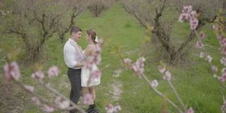 春天，新婚夫妇在树前拥抱。行动。新婚夫妇在自然背景下温柔的一瞥和拥抱。一对新人在春天的树前拥抱