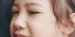 脸近4K可爱的5岁亚洲女孩在妈妈的怀抱中哭泣，透过她的眼睛向人们表达悲伤、不快乐、沮丧和悲伤的情绪。