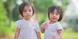 在草坪公园里，一对可爱的亚洲华人双胞胎男婴向他们的父母挥手