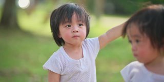 可爱的亚洲华人双胞胎男婴好奇地看着草坪公园里慢跑经过的人们