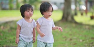 周末早上，一对亚洲华人双胞胎男婴在公园草坪上散步