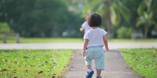 周末早上，一对亚洲华人双胞胎男婴在公园草坪上走向镜头