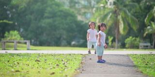 周末早上，一对亚洲华人双胞胎男婴在公园草坪上走向镜头