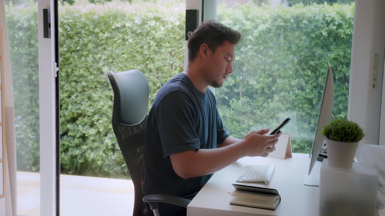 年轻的亚洲自由职业者男子讲手机。休闲集中企业家开发项目，工作时使用电脑坐在家里的办公桌