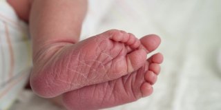 可爱的小婴儿光脚和脚趾头的第一天的生活在白色的背景。靠近小腿干燥的婴儿皮肤婴儿甜蜜地睡在柔软舒适的床上。童年,孕妇的概念