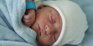 新生儿脸部肖像痤疮过敏刺激早期睡眠在蓝色背景。在帽子上的生命开始分钟的孩子。婴儿，分娩，出生的最初时刻，开始的概念