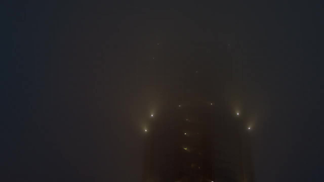 在浓雾中，一幢高层建筑上闪烁着亮光。