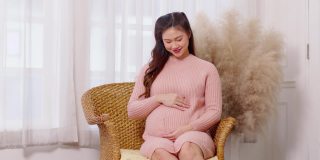 快乐的孕妇坐在沙发上，抱着自己的大肚子在舒适的家里抚摸，年轻的孕妇在家里享受未来生活的放松，母亲和怀孕的概念，柔软的焦点