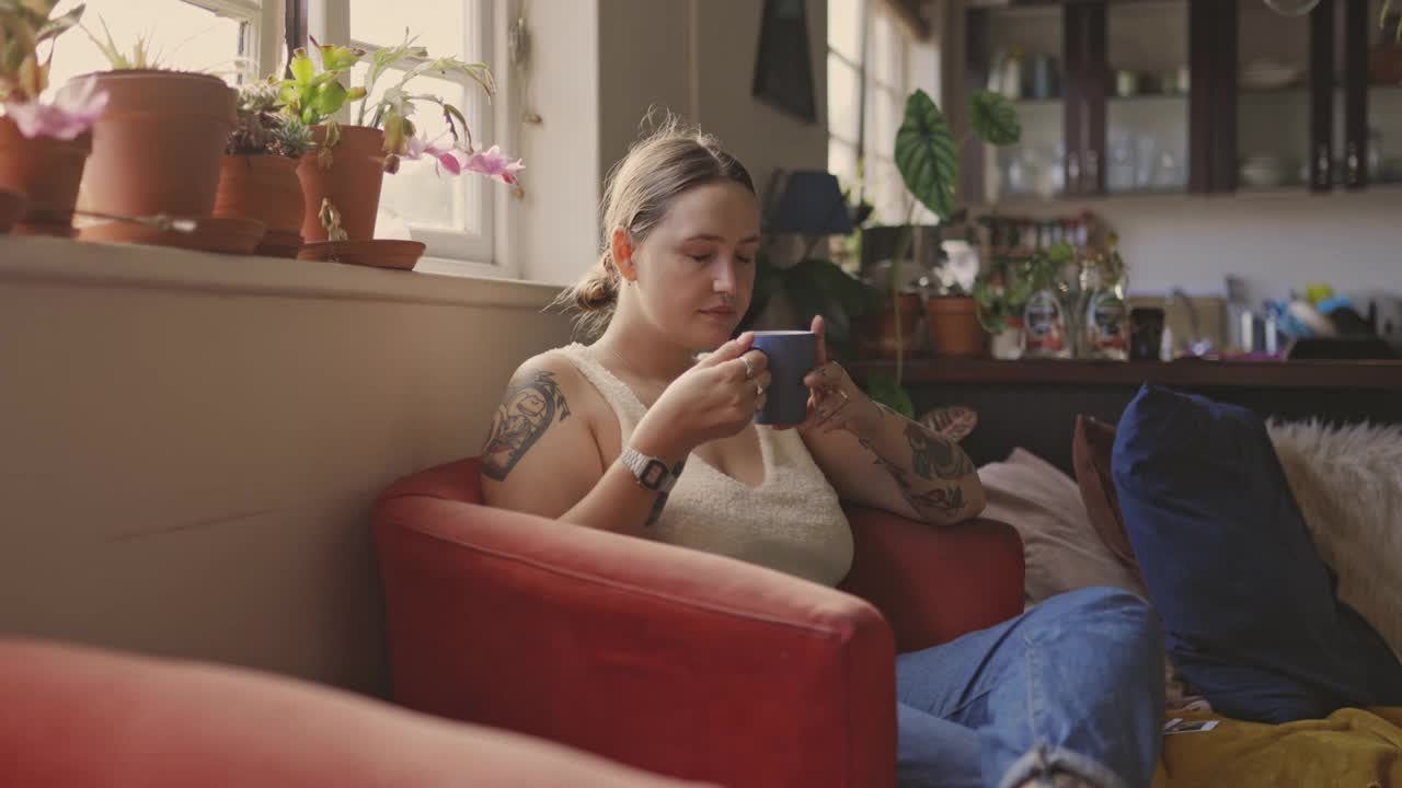 一名年轻女子在家里的沙发上放松地喝咖啡的4k视频片段