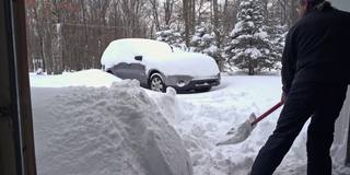 一场冬季暴风雪过后，一名男子正在清理车库和车道的出口。